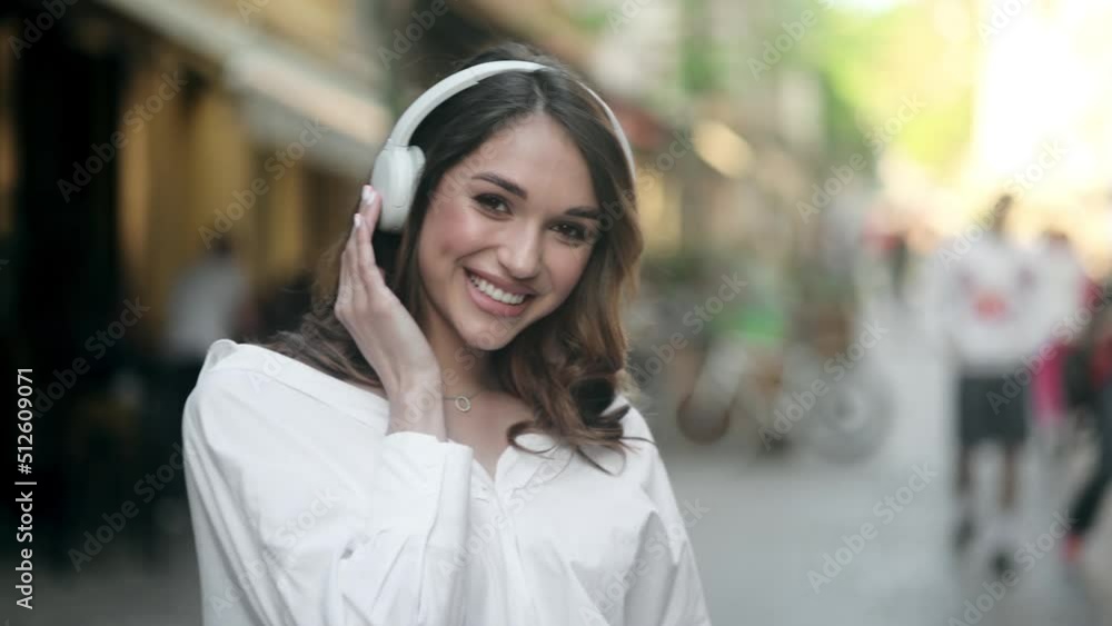 Optimistic girl with brunette hair in white shirt and headphones smiles and dancing outdoors Optimistic girl with brunette hair in white shirt and headphones smiles and dancing outdoors