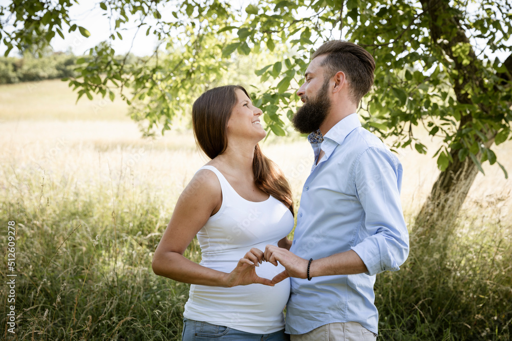 pretty young pregnant woman with white shirt stands with her boyfriend with beard and blue shirt in high flower meadow and cuddle pretty young pregnant woman with white shirt stands with her boyfriend with beard and blue shirt in high flower meadow and cuddle