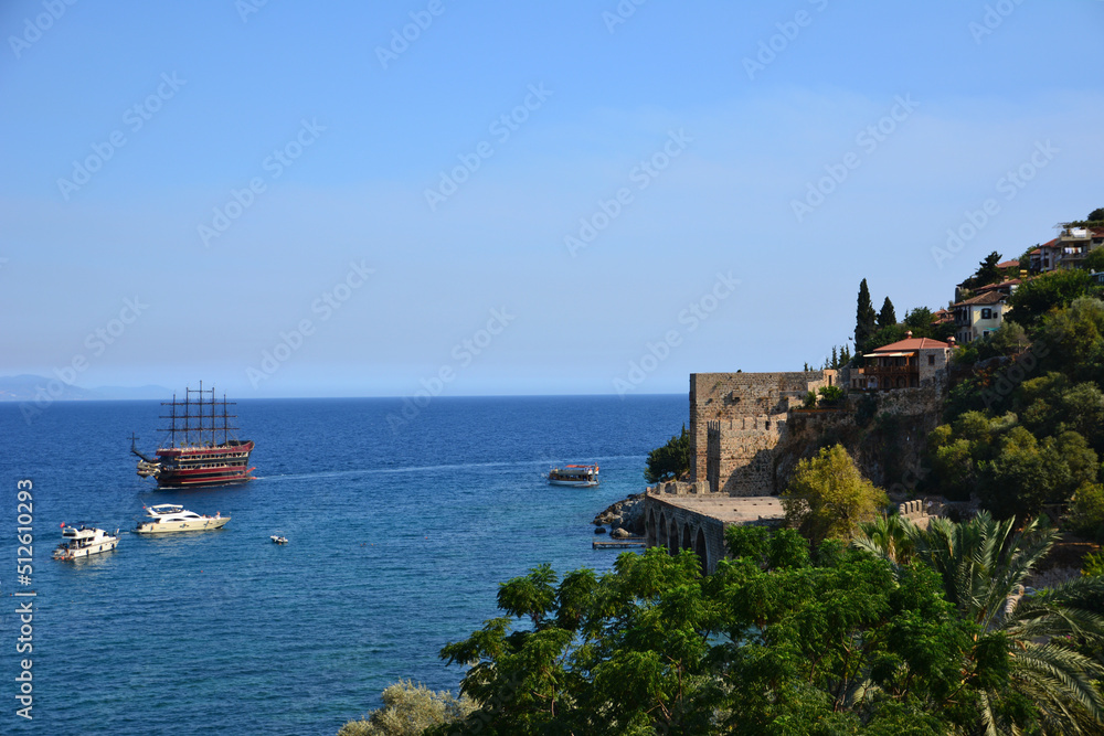 coastline with ancient fortress and trees around and ship on mediterranean sea