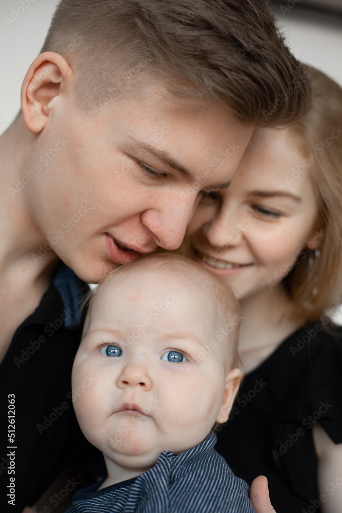 Portrait of young good-looking family in dark clothes with plump cherubic baby infant toddler kiss on white background. Portrait of young good-looking family in dark clothes with plump cherubic baby infant toddler kiss on white background.