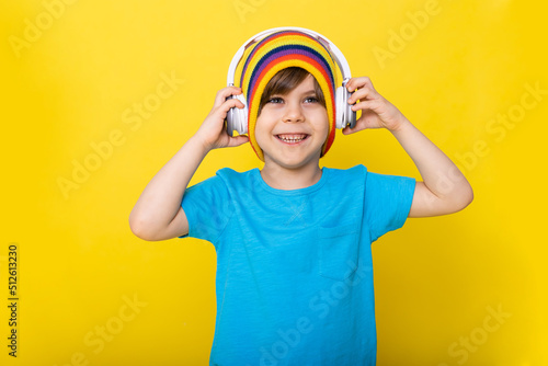 Handsome little boy in blue shirt and colorful hat with headphones, yellow background