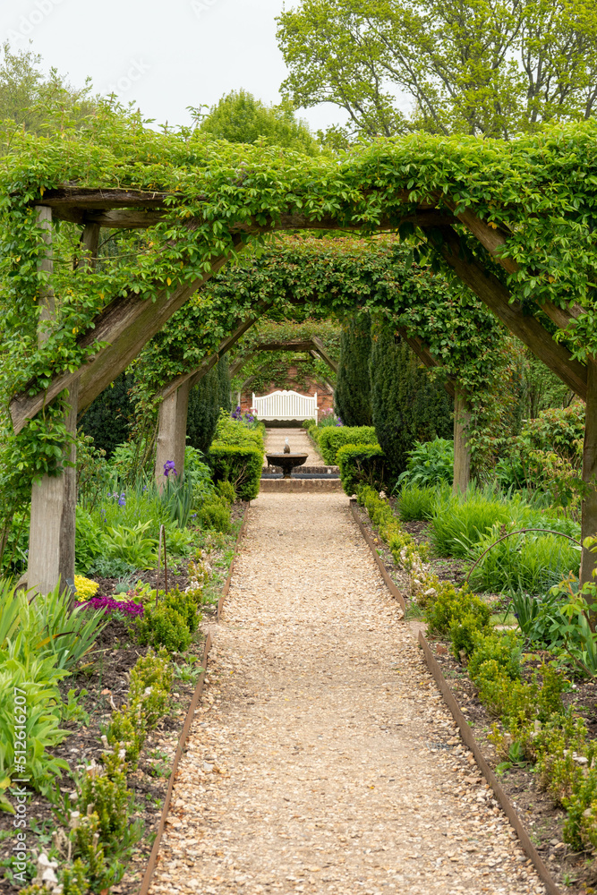 Fototapeta premium Looking down through pergola in the garden towards a water feature and seat 