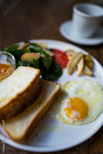 Bread, fried egg and vegetables on a white plate early in the morning