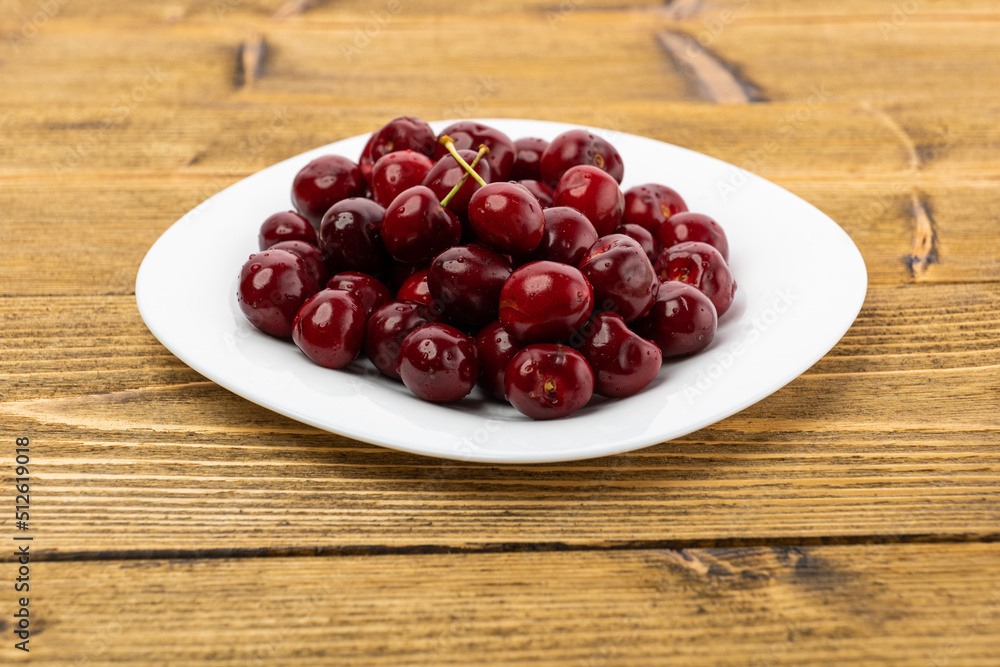 ripe red cherries in a white plate on a wooden background ripe red cherries in a white plate on a wooden background