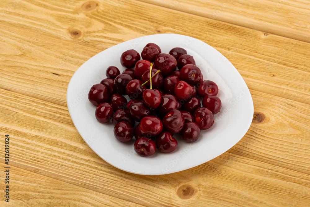 ripe red cherries in a white plate on a wooden background ripe red cherries in a white plate on a wooden background