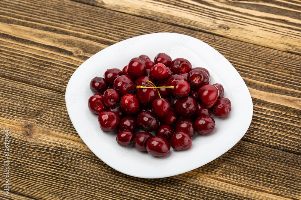 ripe red cherries in a white plate on a wooden background ripe red cherries in a white plate on a wooden background
