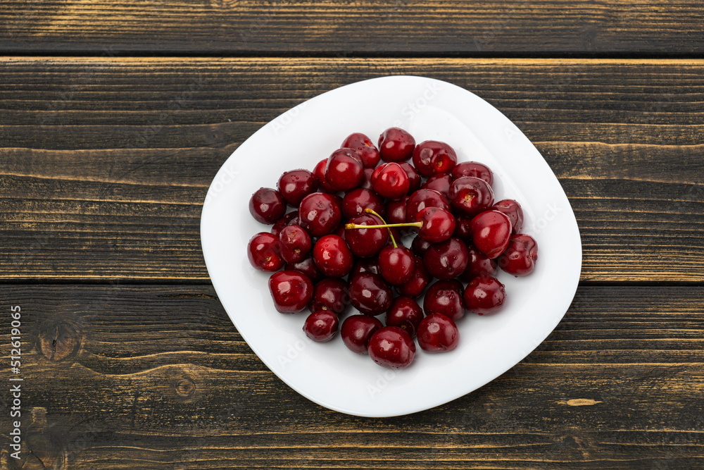 ripe red cherries in a white plate on a wooden background ripe red cherries in a white plate on a wooden background