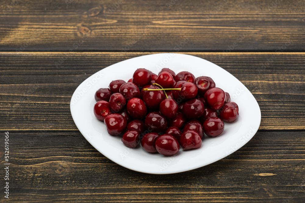 ripe red cherries in a white plate on a wooden background ripe red cherries in a white plate on a wooden background