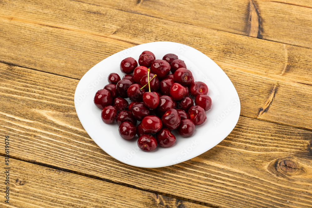 ripe red cherries in a white plate on a wooden background ripe red cherries in a white plate on a wooden background
