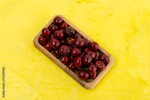 ripe red cherries in a wooden bowl on a yellow background