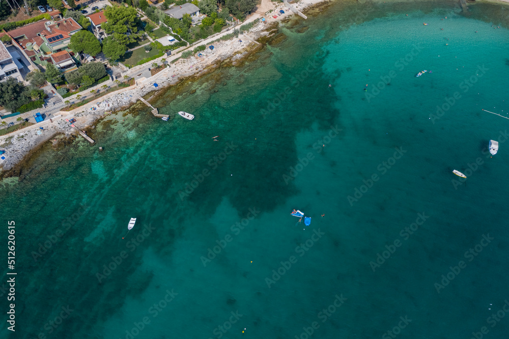 Top aerial view of a rock beach with beautiful blue green water in Rovinj on the Mediterranean sea with road and buildings on the coast