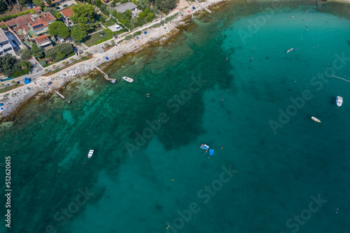 Top aerial view of a rock beach with beautiful blue green water in Rovinj on the Mediterranean sea with road and buildings on the coast © TambolyPhotodesign