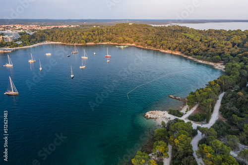 Fototapeta Naklejka Na Ścianę i Meble -  Aerial view of a beach with turquoise blue green sea water of the adriatic sea by sunset, Rovinj, Croatia 