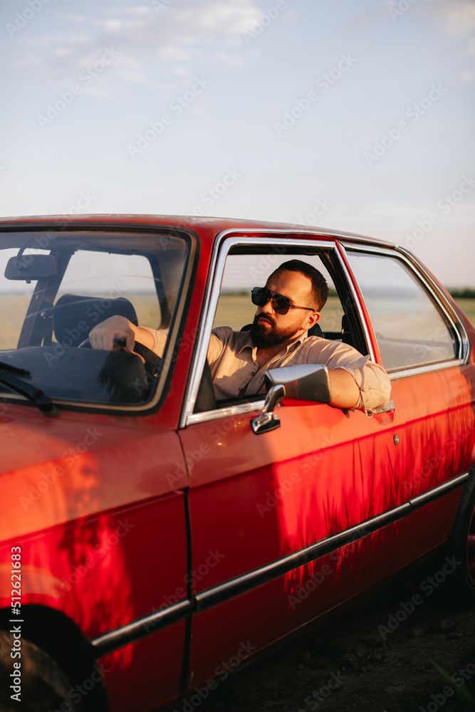 A young man with beard in sunglasses travels inside red retro car. A young man with beard in sunglasses travels inside red retro car.