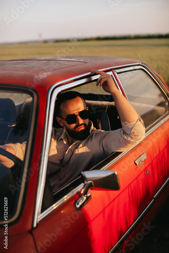 A young man with beard in sunglasses travels inside red retro car.  © VikaNorm