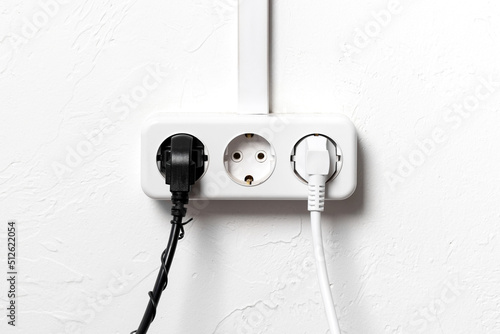 Group of white european electrical outlets with two plugs inserted into it on white concrete wall