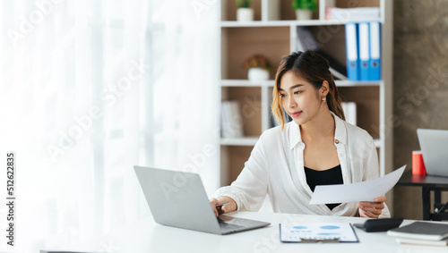 Beautiful young woman using laptop and smiling while working in office, business concept.