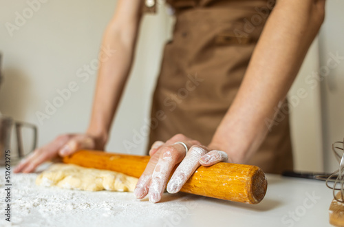 A woman in a special apron cooks at home. Rolling out and preparing dough for baking.