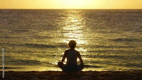 Beautiful silhouette of free woman sitting in meditation pose on beach at golden sunset. Lotus position, medicine yoga asana balance kundalini energy, practice good for woman health and mindfulness photo