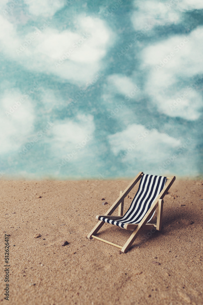 View of a blue and white deck chair on sand. Blue sky background with white fluffy clouds View of a blue and white deck chair on sand. Blue sky background with white fluffy clouds