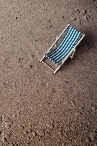 Angled view down onto a blue and white deck chair surrounded by sand. Copy space available