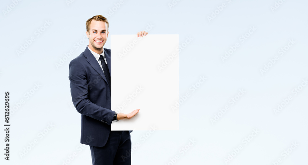 Happy smiling business man in suit, necktie showing advertising mock up sign board, empty banner with copy space for ad text or slogan, isolated on grey background. Businessman hold blank white paper. Happy smiling business man in suit, necktie showing advertising mock up sign board, empty banner with copy space for ad text or slogan, isolated on grey background. Businessman hold blank white paper.
