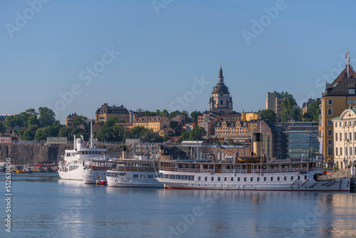 New and old steam boats at the pier Skeppsbron in the district Gamla Stan and the church Katarina with old yellow 1700s houses a summer day in Stockholm photo
