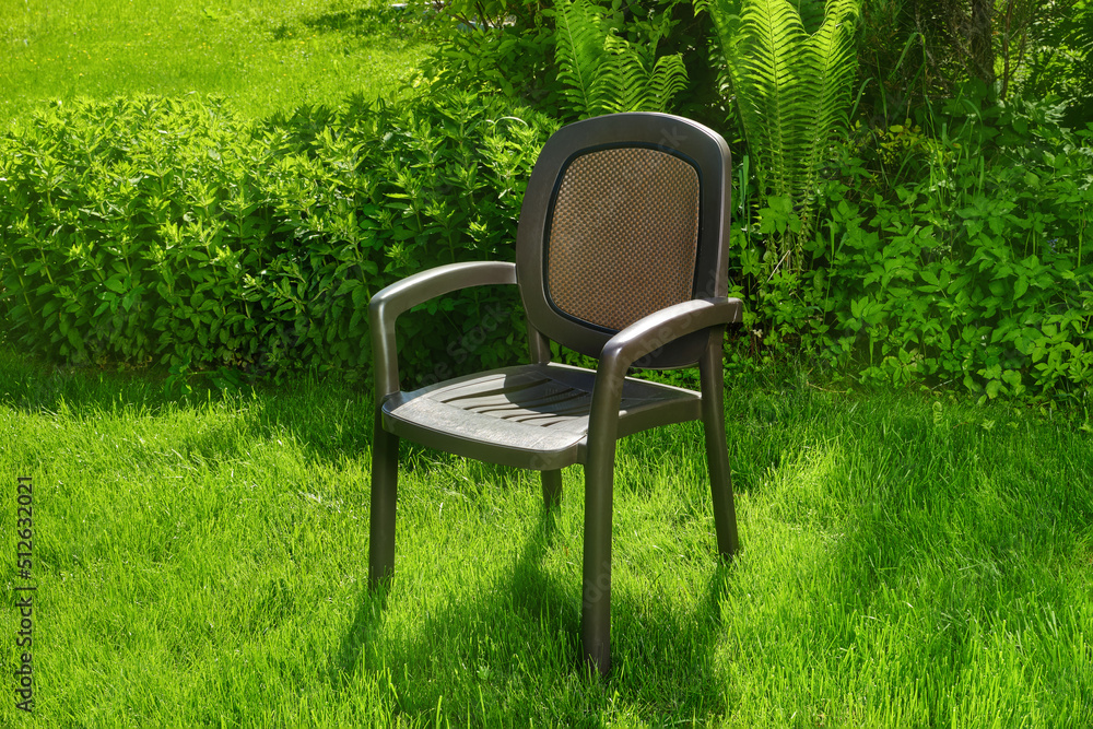 Single chair in the garden. Plastic chair in ornamental garden background. Selective focus. Single chair in the garden. Plastic chair in ornamental garden background. Selective focus.