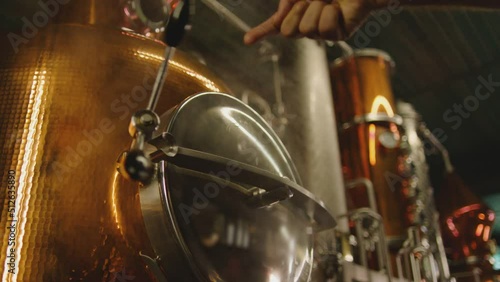 Professional big factory of alcohol drinks . Man's hand opening door of tank . Vodka wine tequilla production filtration , distillation . Alcohol preparation . Close up making alcohol . Boiler , steam