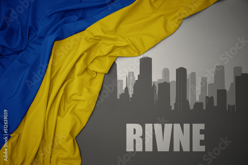 abstract silhouette of the city with text Rivne near waving national flag of ukraine on a gray background. photo