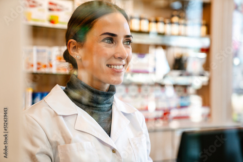 White apothecary wearing lab coat smiling while working in pharmacy photo