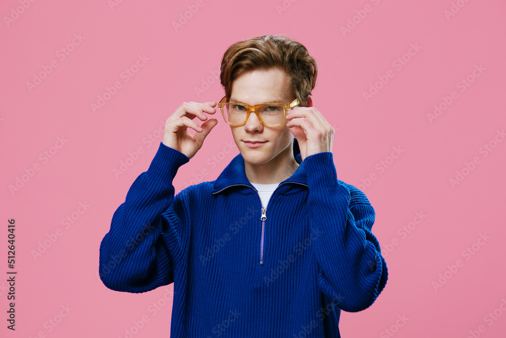 portrait of a guy adjusting his orange-rimmed glasses, standing in a blue sweater on a pink background portrait of a guy adjusting his orange-rimmed glasses, standing in a blue sweater on a pink background
