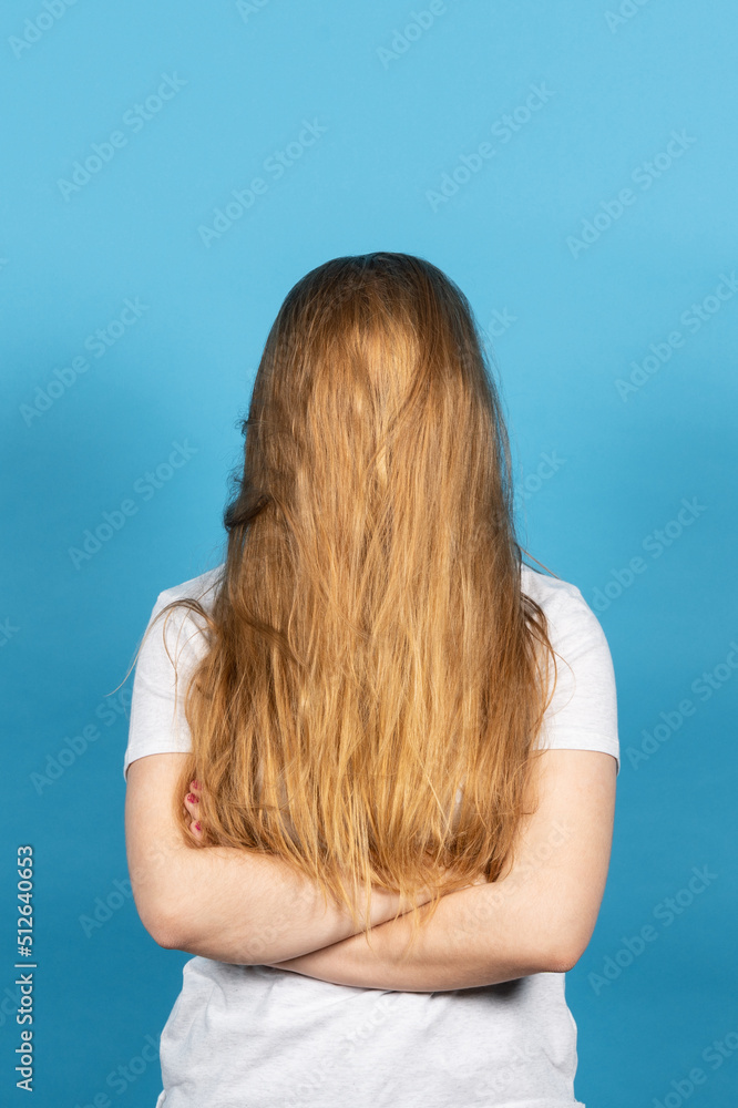 Blonde woman covering face with long hair isolated on blue background.. Hairdressing and hiding identity concept Blonde woman covering face with long hair isolated on blue background.. Hairdressing and hiding identity concept