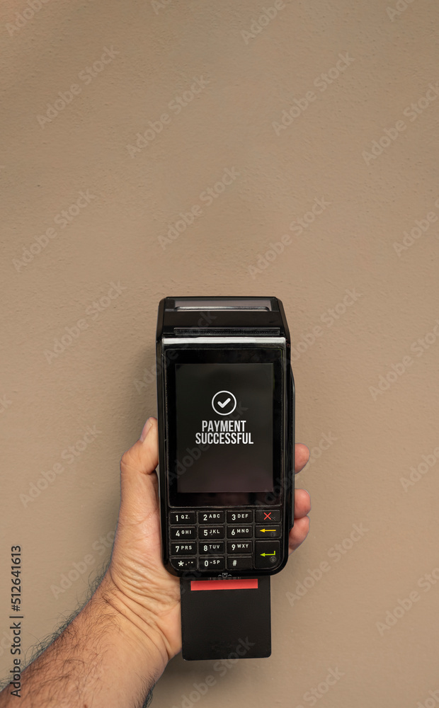 Credit or debit card terminal in hand isolated on light brown background. Close up of POS terminal in hand processing a pay. Copy Space Credit or debit card terminal in hand isolated on light brown background. Close up of POS terminal in hand processing a pay. Copy Space