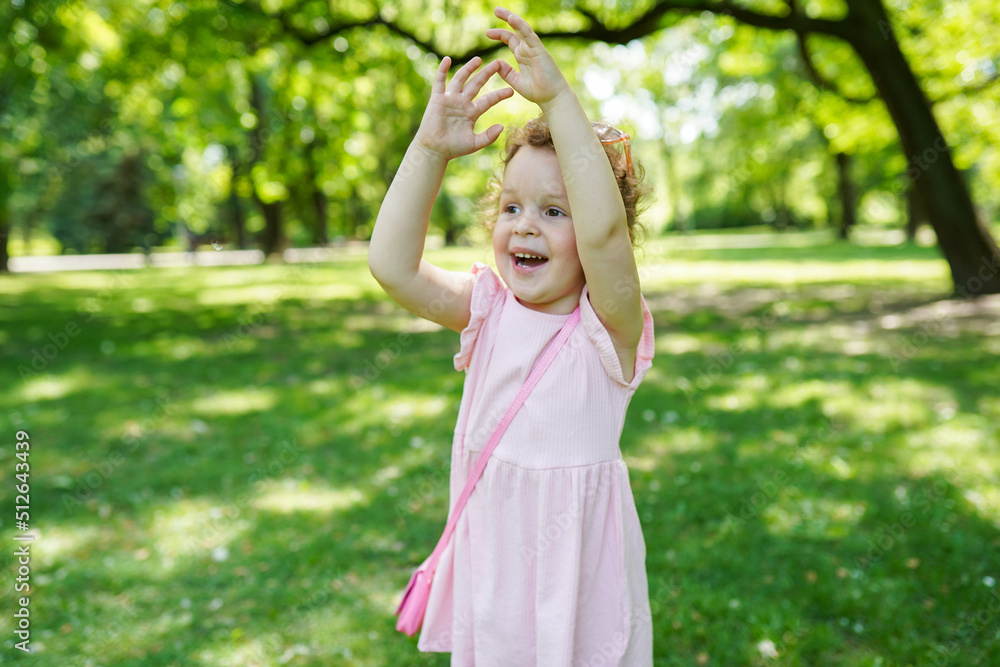 Small attractive lovely cheerful girl in pink dress have fun and walking in the park