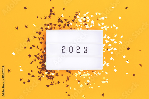 New 2023 Year concept. Lightbox and golden stars confetti on a yellow background.