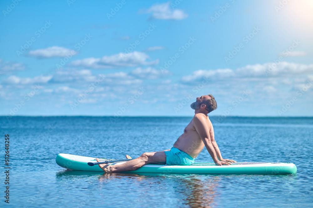 Man sitting meditating on paddle board on water