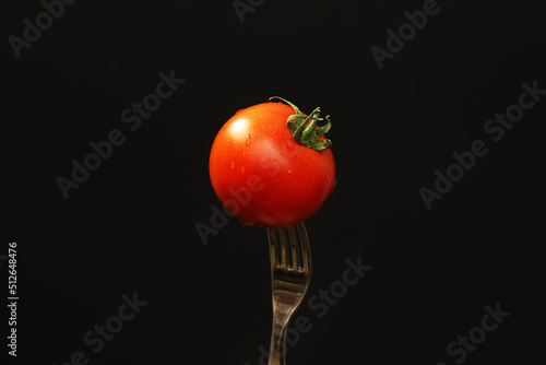 Ripe tomato on a fork on a black background. Close-up