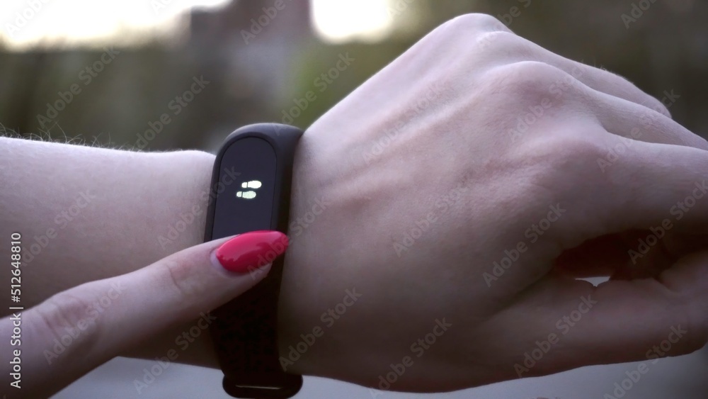 Young woman using wearable fitness tracker. The smart band with display touchpad and heart rate monitor. Entertainment and technology concept. Close-up shot of woman hand with smart watches