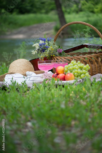 view of delicious snacks, fruits, lemonade and wine on the cover on green grass near the river.
