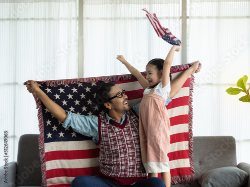 Happy family, Single father and cute little daughter sitting on sofa at home with flags of United States of America, celebrating independence Day. 4th of July, Patriotic US holiday, photo