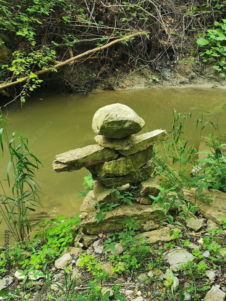 Inukshuk standing on edge of river with beautiful greenery surrounding it. Inukshuk standing on edge of river with beautiful greenery surrounding it.