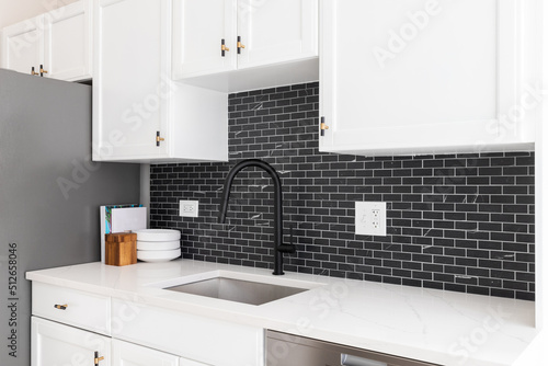 Kitchen sink detail shot with white cabinets, small black marble subway tile backsplash, and a black faucet.