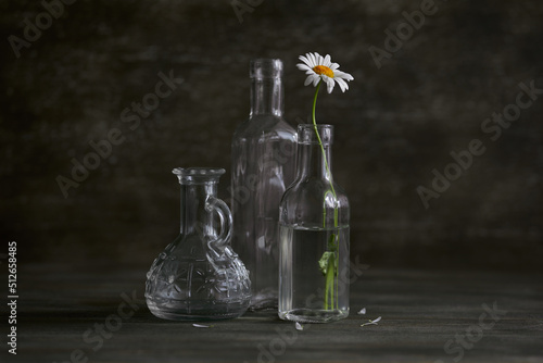 Still life. Single camomile in a glass on a wooden table. Rustic style.