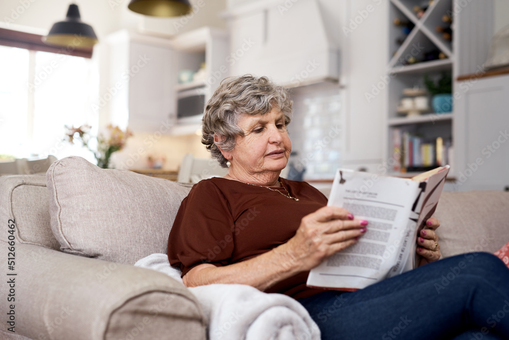 Chosen chapter of contentment. Shot of an elderly woman relaxing with a book on the sofa at home.