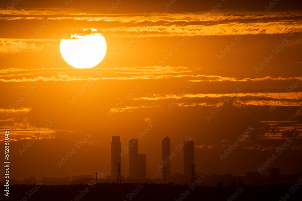 Obraz premium The sun sets during de summer solstice with the view of the skyscrapers and skyline of Madrid.