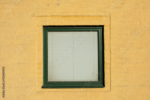 Green window with blinds on yellow plastered old wall © ankihoglund