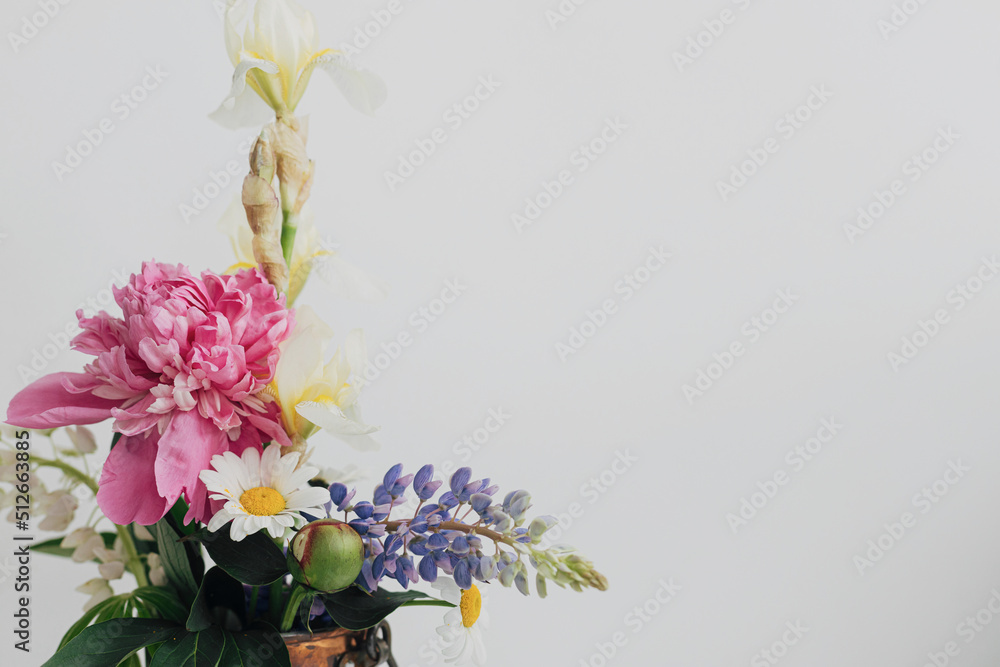 Modern summer flowers still life arrangement on white wall background with space for text. Creative floral greeting card. Stylish peony, lupin, iris and daisy composition