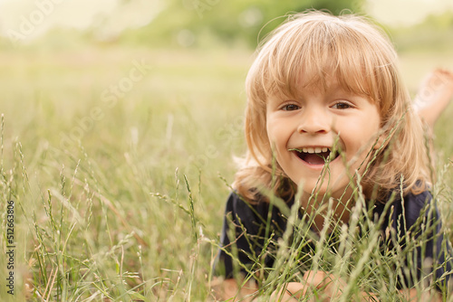 happy little boy curly blond lying on a green lawn summer nature