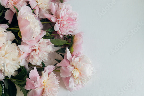 Fototapeta Naklejka Na Ścianę i Meble -  Beautiful peonies flat lay on rustic white wood. Stylish floral greeting card with space for text. Gentle pastel pink peony flowers arrangement on white table, moody banner
